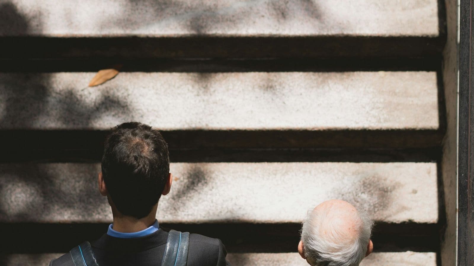 An adult walks beside an older man as they climb outdoor steps