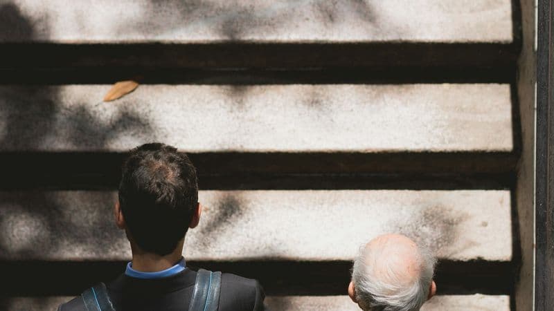 An adult walks beside an older man as they climb outdoor steps