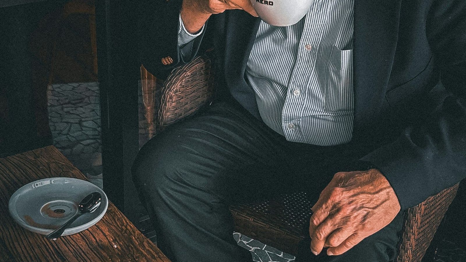 An older man sits in an armchair holding a warm drink