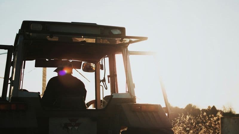 A farmer drives a tractor through a field in late-afternoon light