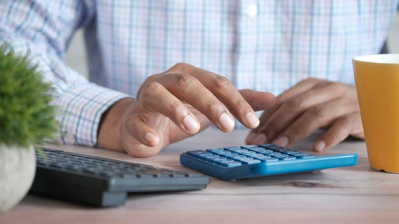 A person calculates figures beside a laptop and coffee cup