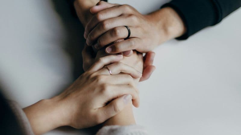 Several people place their hands together in a gesture of support