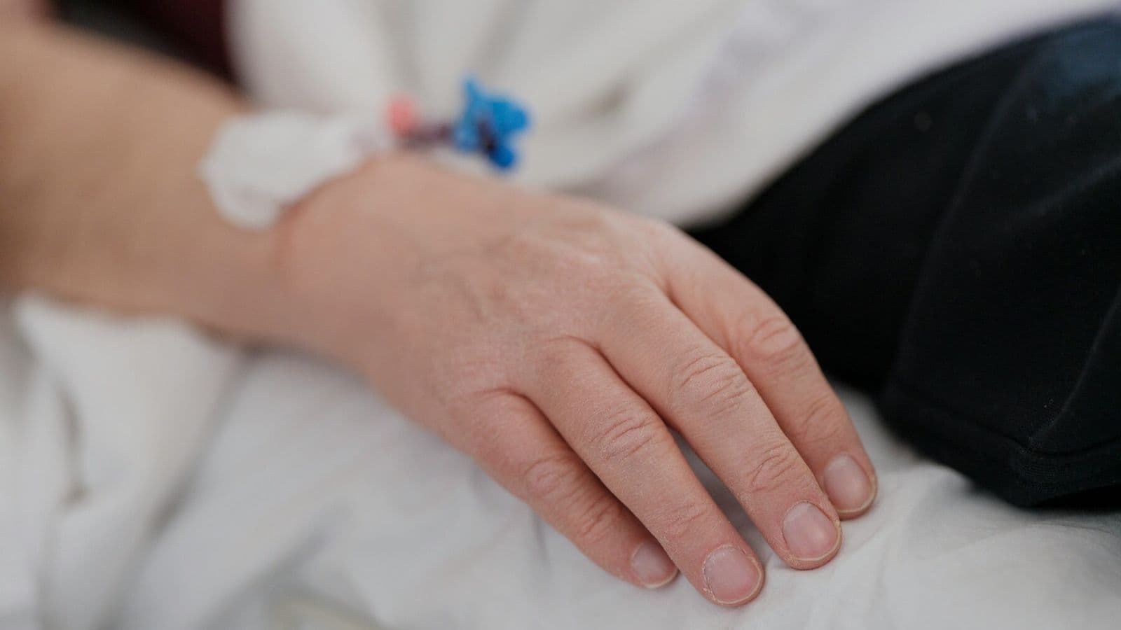 A patient’s hand rests on a hospital bed beside an intravenous line