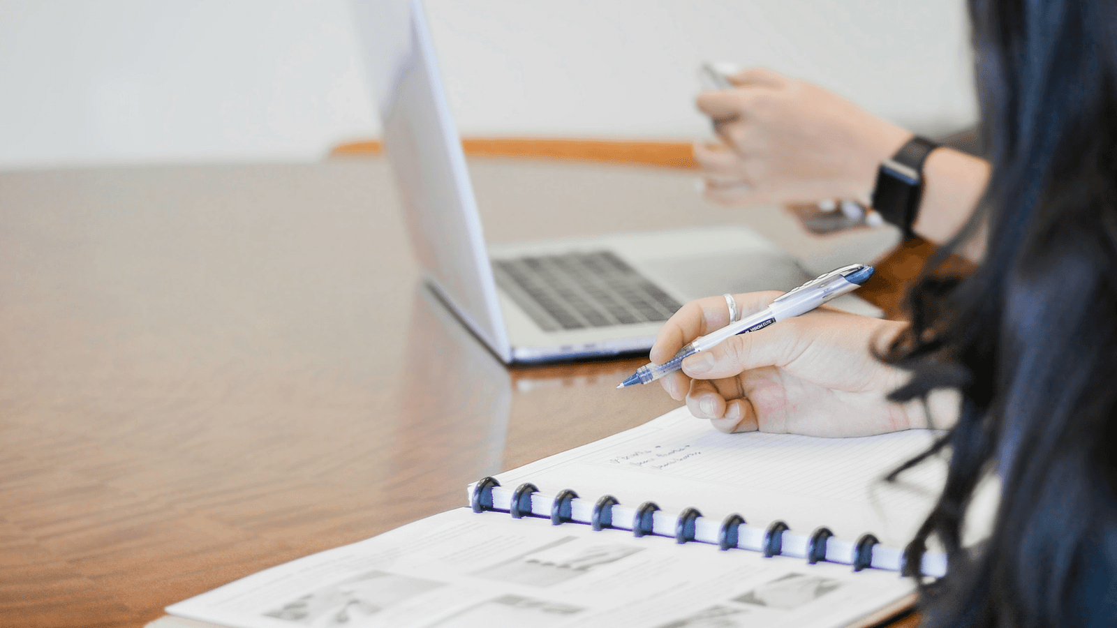 A person writes notes beside a laptop and printed documents