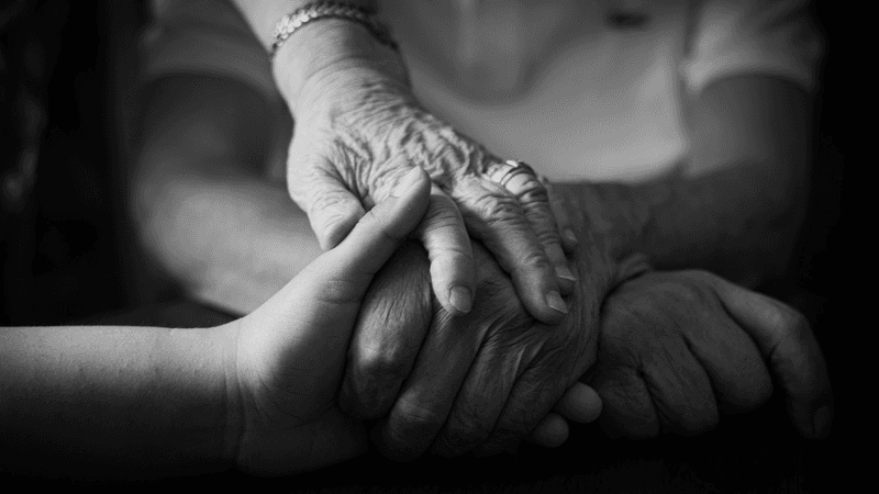 Younger hands gently cradle the hands of an older person