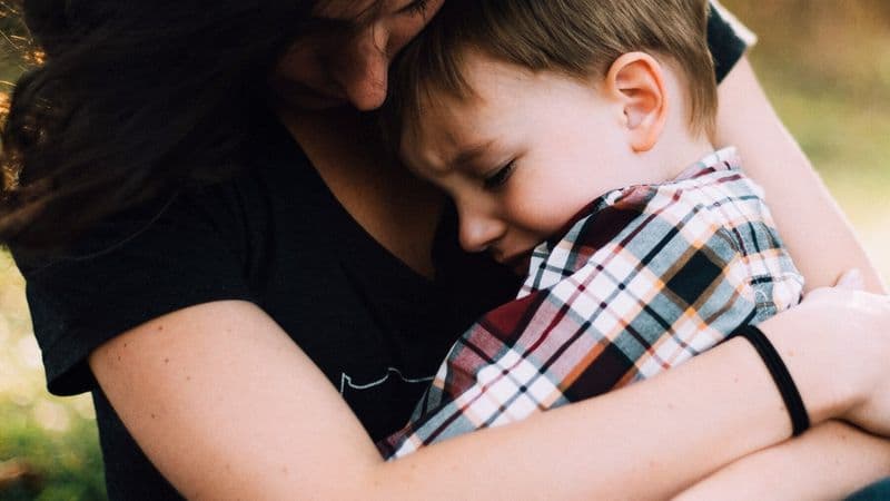A mother holds a grieving child close outdoors