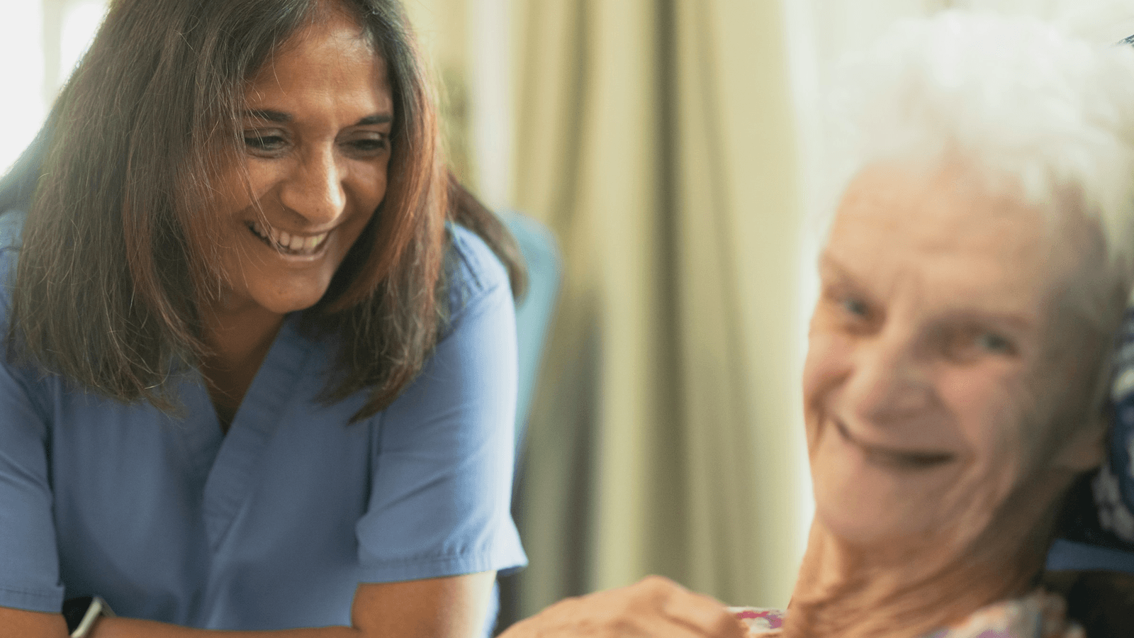 A nurse smiles while speaking with an older woman in a care setting