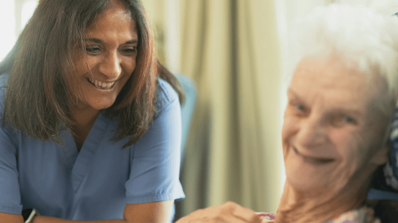 A nurse smiles while speaking with an older woman in a care setting