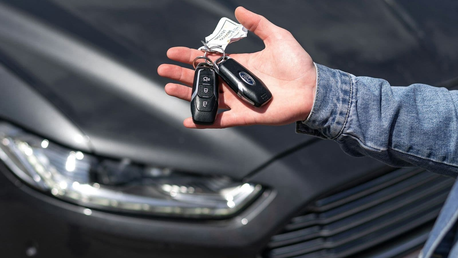 A person holds out a set of car keys beside a parked vehicle
