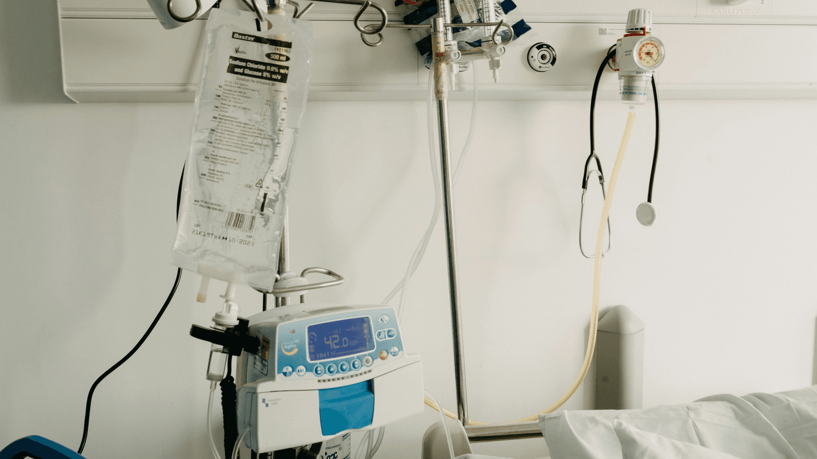 An empty hospital bed beside intravenous fluids and medical equipment
