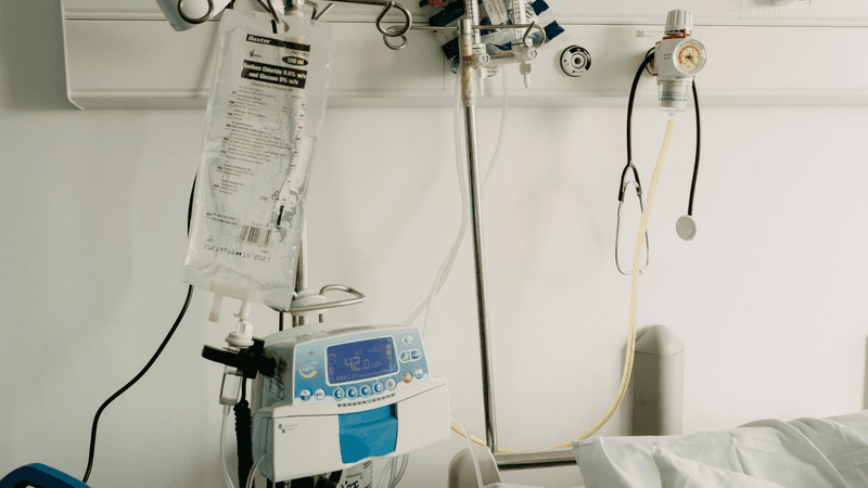 An empty hospital bed beside intravenous fluids and medical equipment